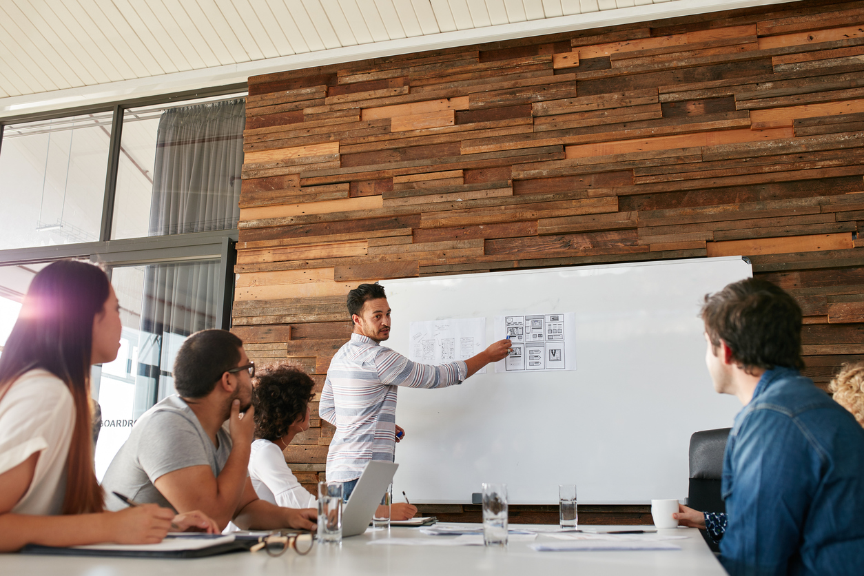 Portrait of young businessman giving presentation to colleagues. Young man showing new app design layout on white board to coworkers during business presentation.